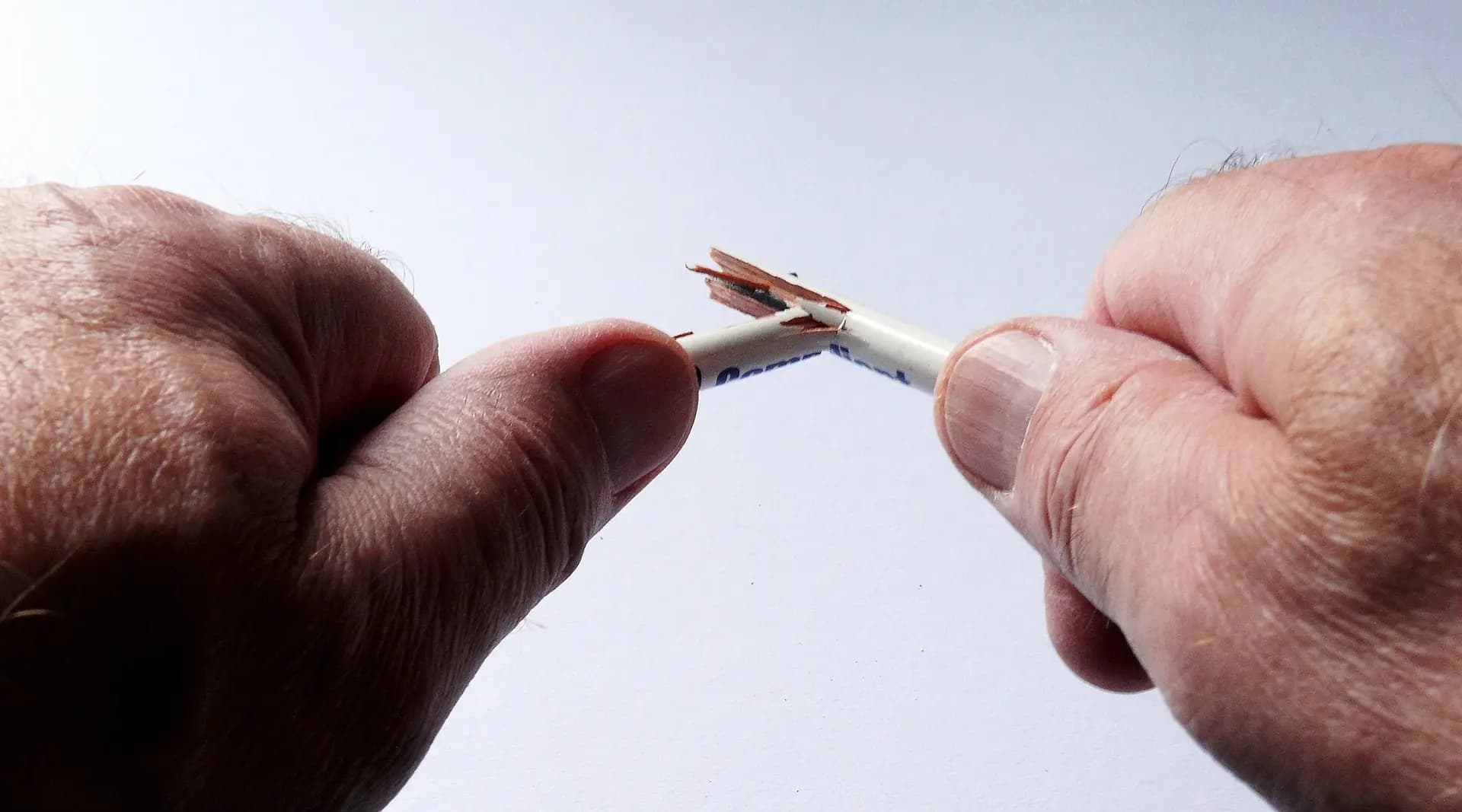 Hands breaking a pencil in frustration, symbolizing writer’s block and creative struggle